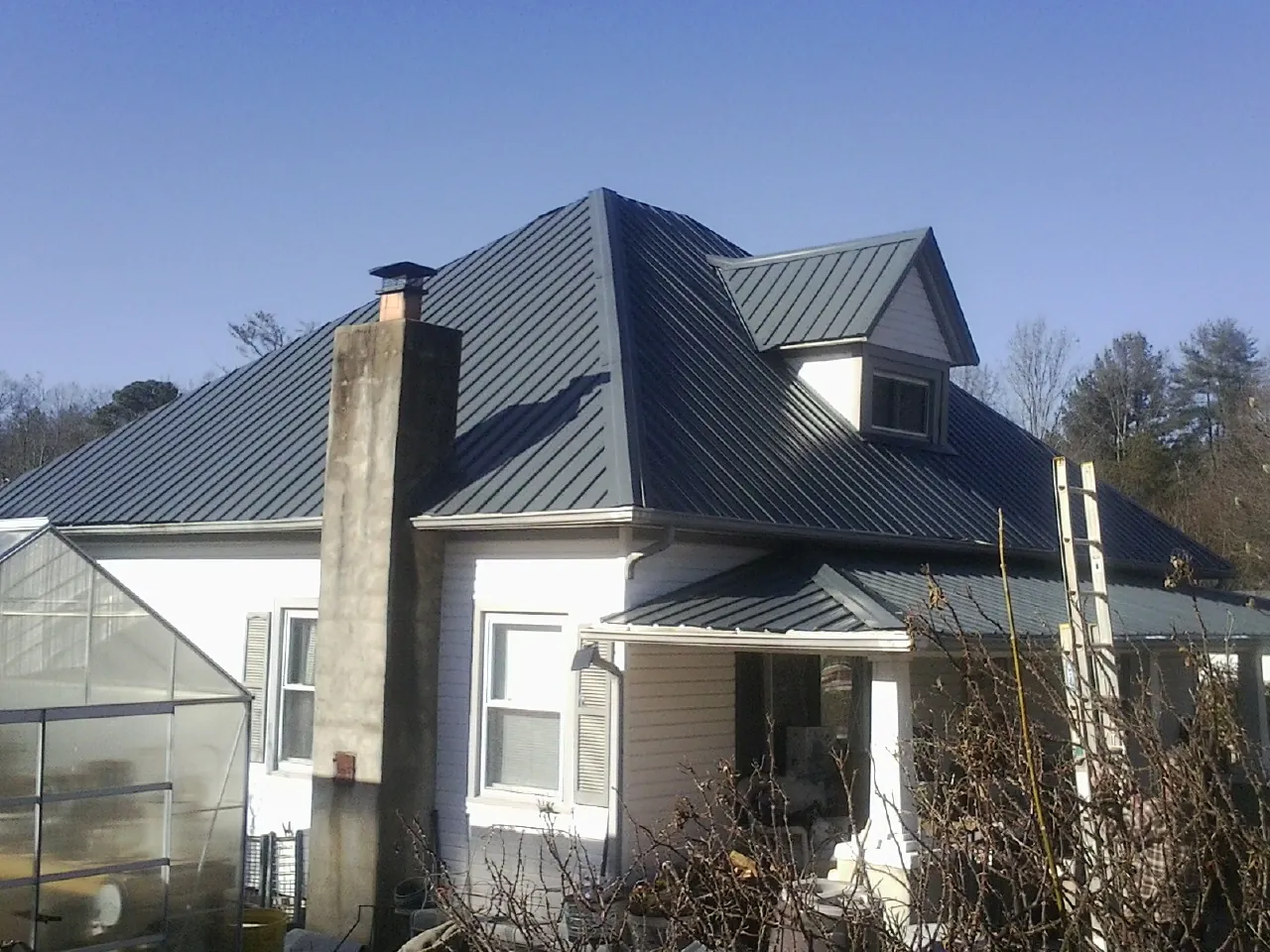 Dark blue standing seam metal roof on a white farmhouse with dormer — Slate & Tile Roof Repair by Roofing Brothers in Honea Path