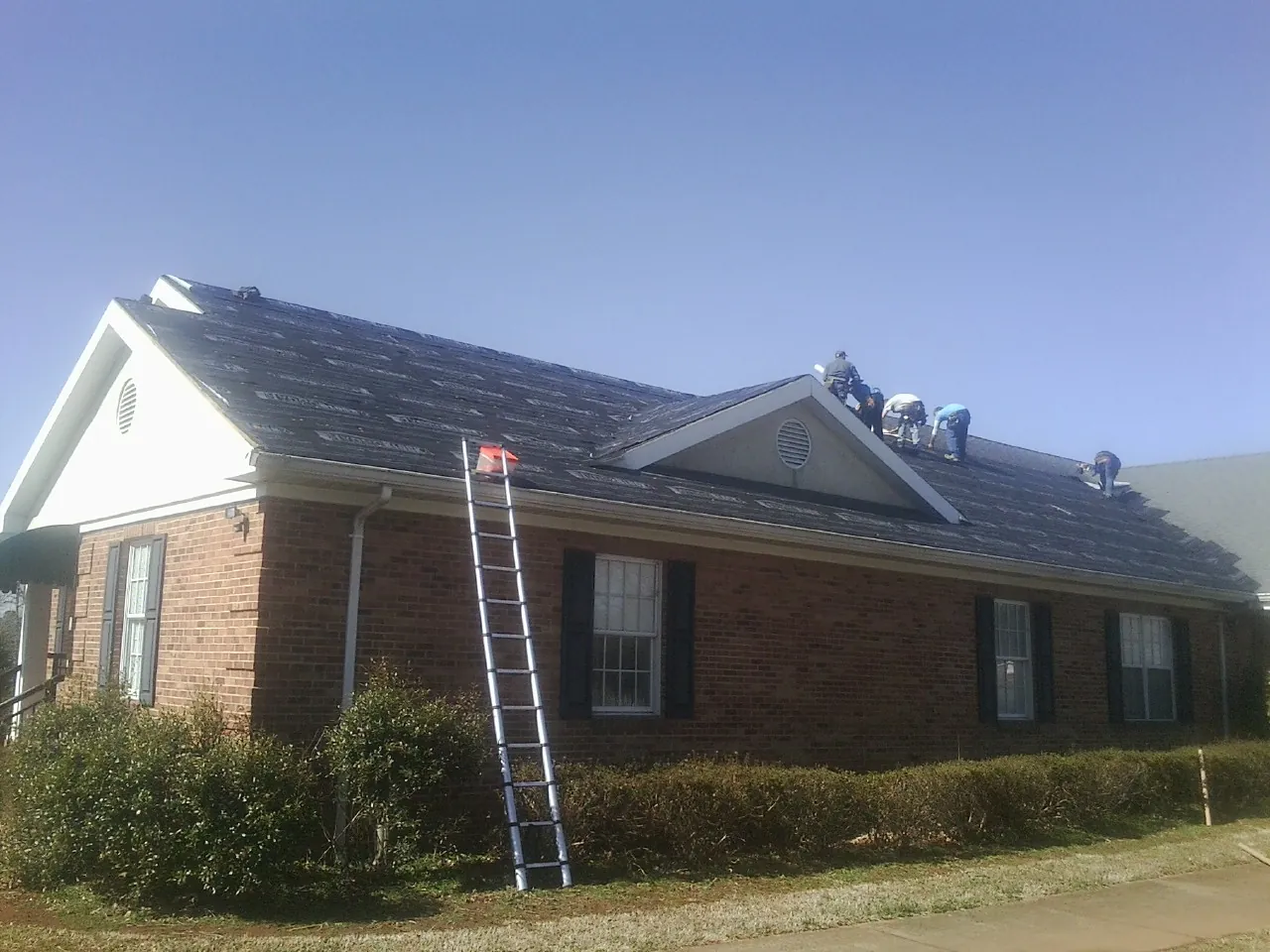 Crew tearing shingles off a brick ranch roof with a ladder set — Emergency Roof Repair work by our crew in Honea Path