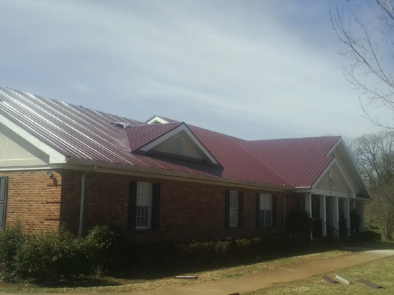 Red metal roof with gabled entries on a long brick building, from a Hail Damage Roof Repair job in Honea Path
