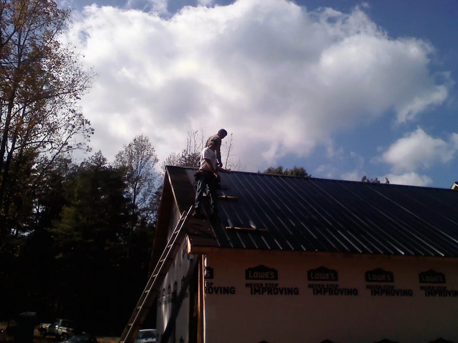 Roofer fastening dark metal panels high against a cloudy sky, from a Roof Inspection job in Honea Path